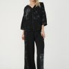 femeie purtând un set casual negru cu jachetă cu glugă și pantaloni largi, ochelari de soare si sandale negre