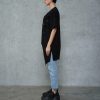 vedere din lateral, femeie cu tricou asimetric negru cu umăr decupat, blugi si sneakers negri cu platformă