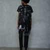 vedere din spate, femeie purtând un set urban negru cu bluză asimetrică și pantaloni conici cu cizme cu toc negre