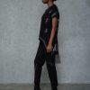 vedere din lateral, femeie purtând un set urban negru cu bluză asimetrică și pantaloni conici